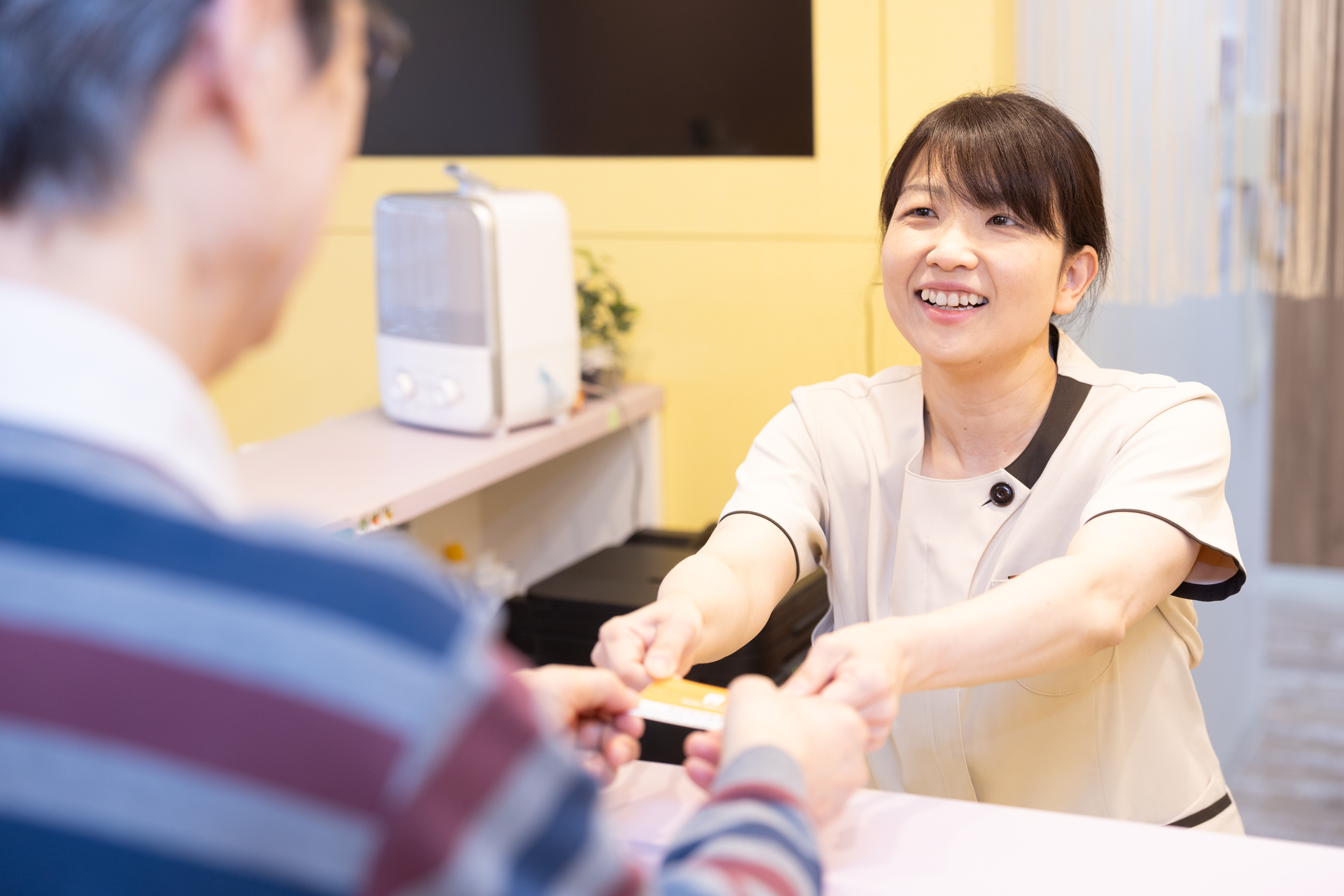 新生歯科医院の受付スタッフが患者さんに笑顔で応対している様子